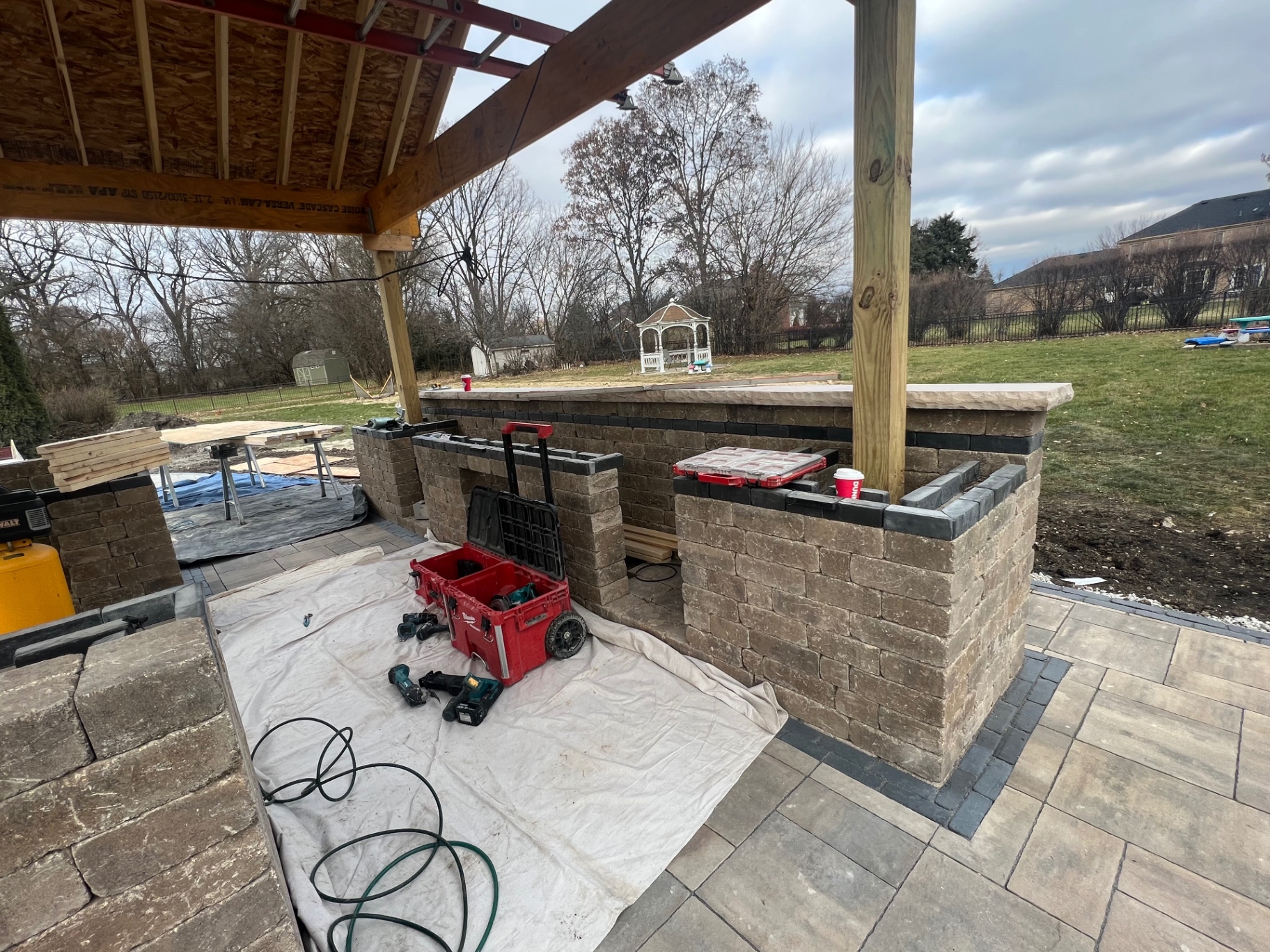 Outdoor kitchen build-out with stone bar walls and capstones under a wood pavilion